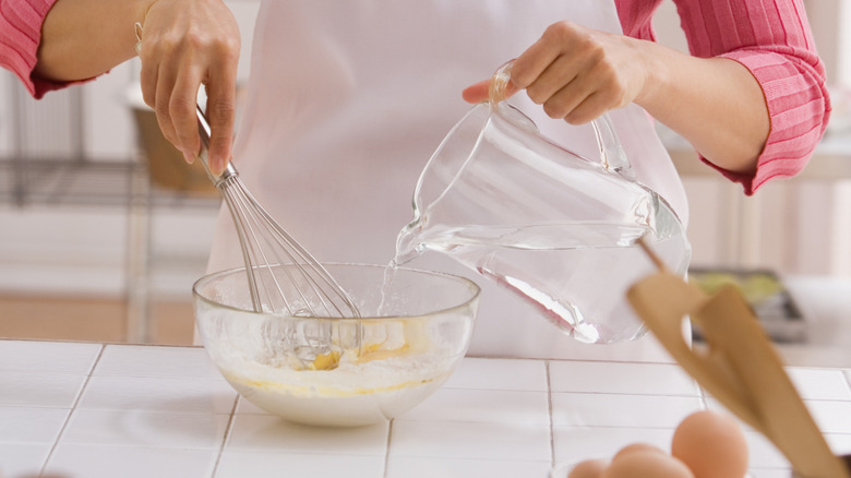 Woman pouring cold water into cake batter.