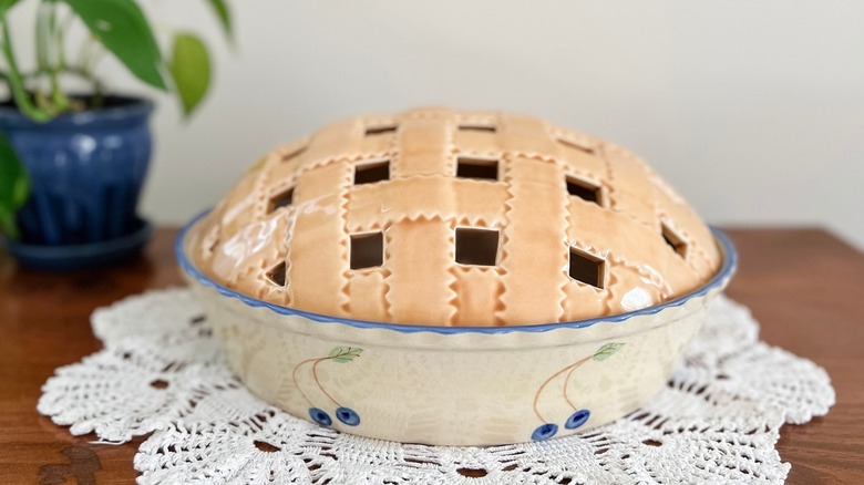 A ceramic pie holder painted with blueberries and a lid that looks like a latticed pie top