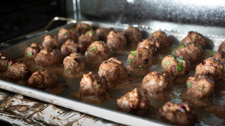 A baking sheet full of meatballs is placed on a rack inside an oven.