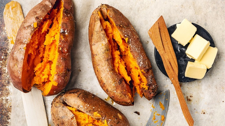 Whole baked sweet potatoes cut down the middle next to a small plate with pats of butter