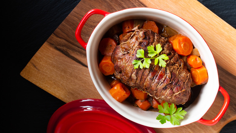 Veal pot roast in a Dutch oven on a black background.