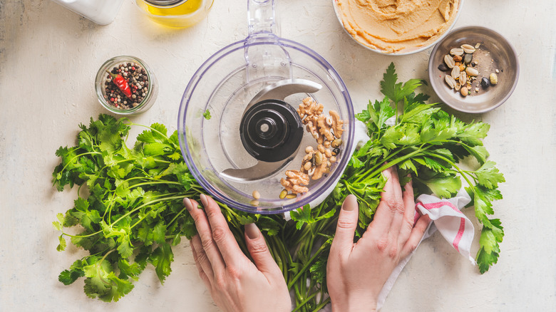 A woman's hands are seen around the bowl of a food processor surrounded by ingredients.