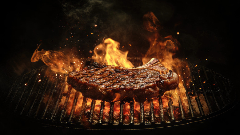 A steak cooking on a grill with flames around it