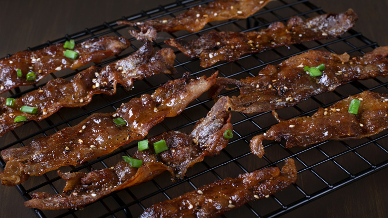 Candied bacon slices topped with spices and green onions on a black cooling rack