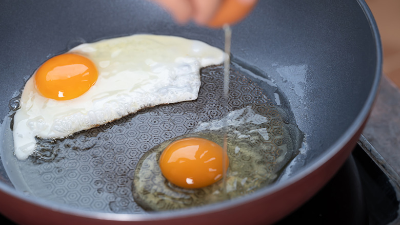 Hand cracking a fresh egg into a frying pan for fried egg