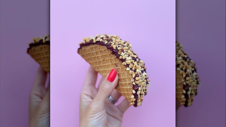 A hand holding a homemade Choco Taco in front of a light purple wall