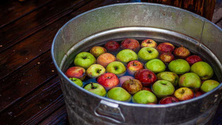 A large metal basin filled with water and red and green apples for bobbing.