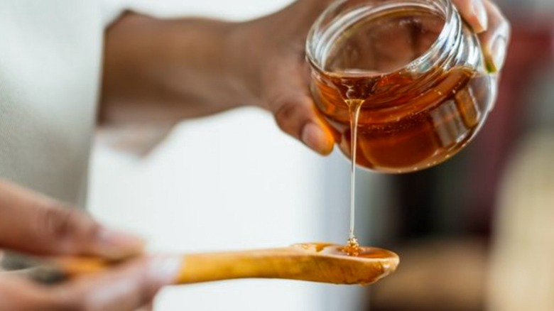 Woman pouring honey onto mixing spoon