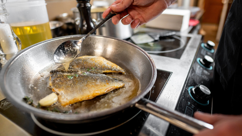 Fish filets cooking skin-side-up in a stainless steel pan as chef bastes with butter