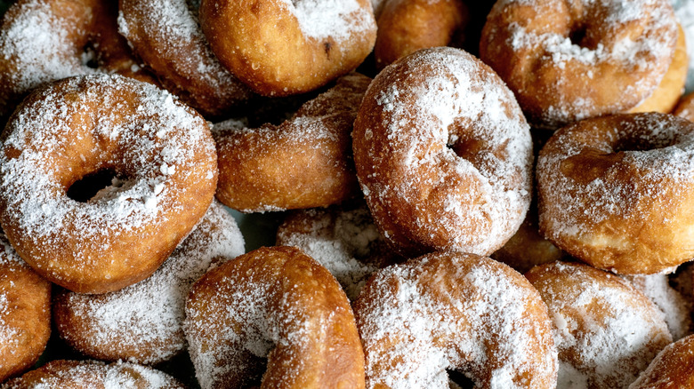 Perfectly brown donuts sprinkled with powdered sugar are stacked on top of each other