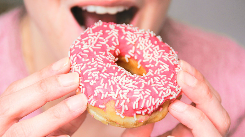 A person about to take a bite of a donut with pink icing and white sprinkles