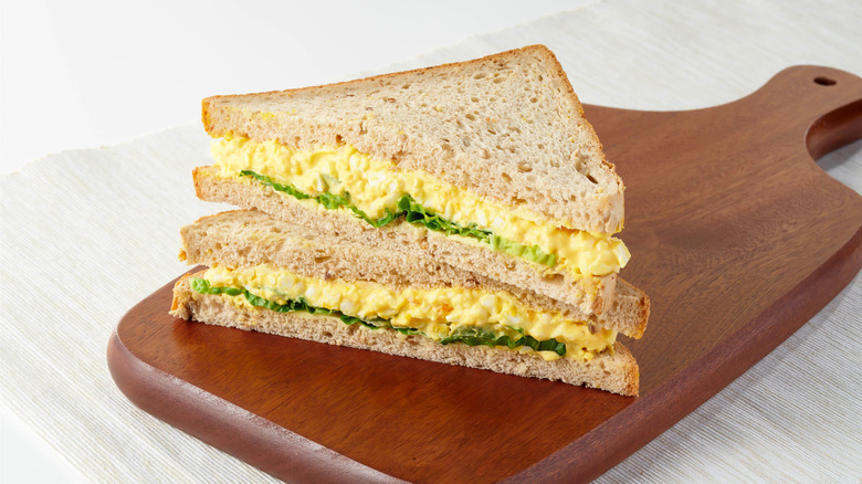 Egg salad sandwich cut in half on wooden cutting board.