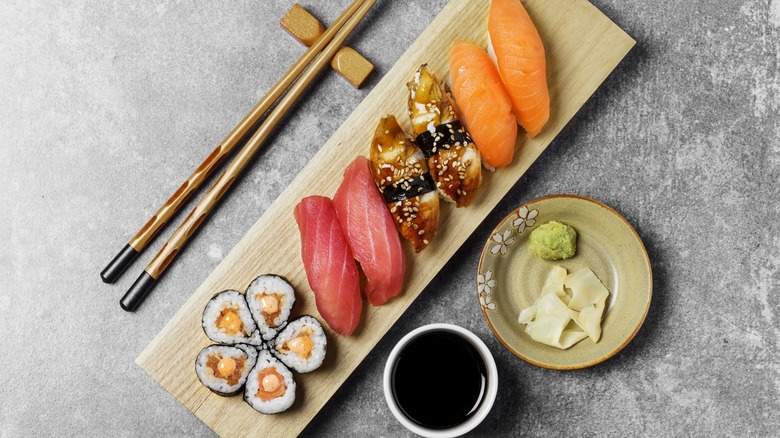 sushi on a wooden platter with chopsticks, soy sauce, wasabi, and gari on the side