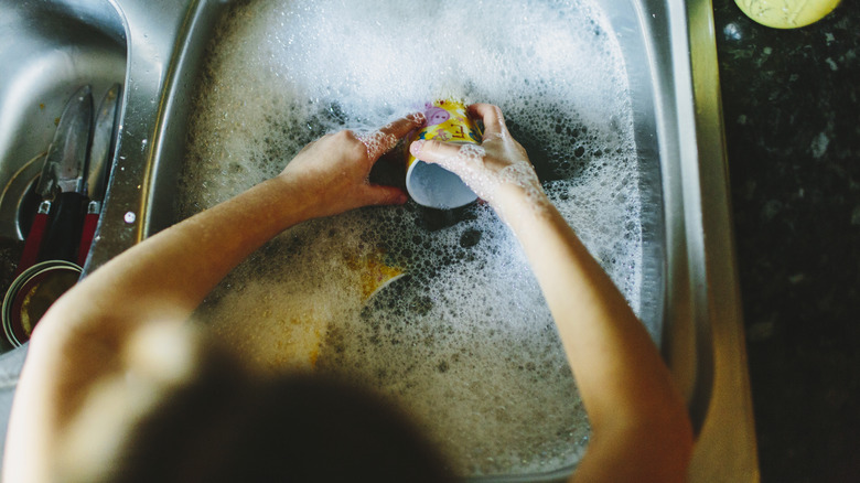 Hands wash a mug in a sink filled with soapy water