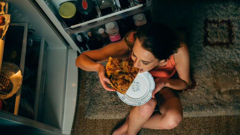 woman eating cold pizza from fridge