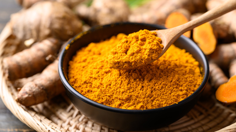 Ground turmeric powder powder in a black bowl with a wooden spoon