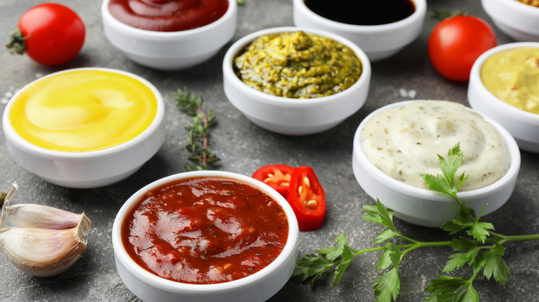 Many different sauces and spices are arranged on a gray surface.