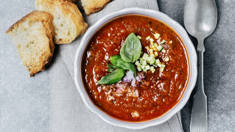 Tomato soup in white bowl with white bread on a grey table