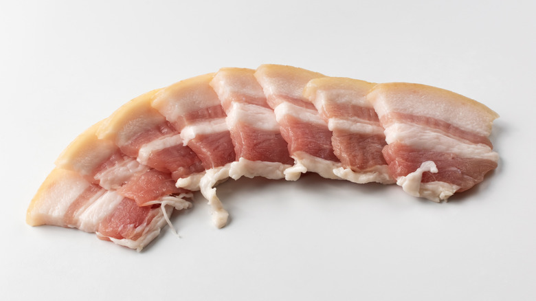 Slices of raw bacon on white table