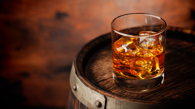 A glass of scotch with ice on a whisky barrel