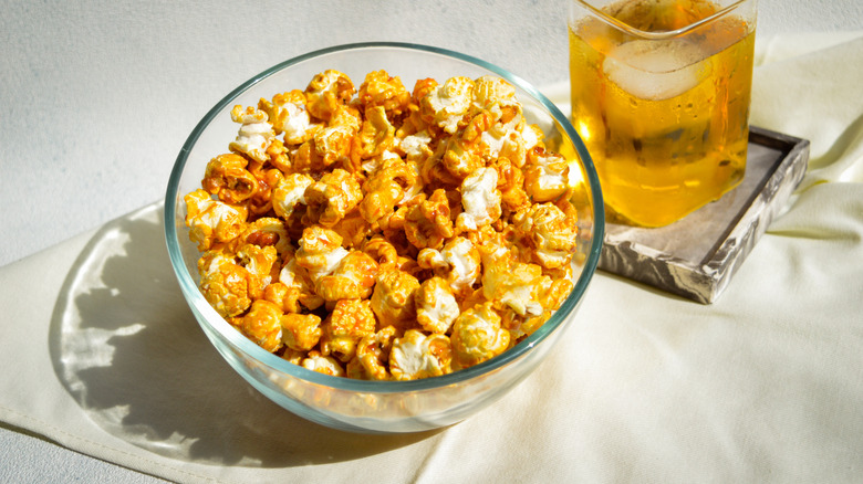 A glass bowl of popcorn with a drink in the background