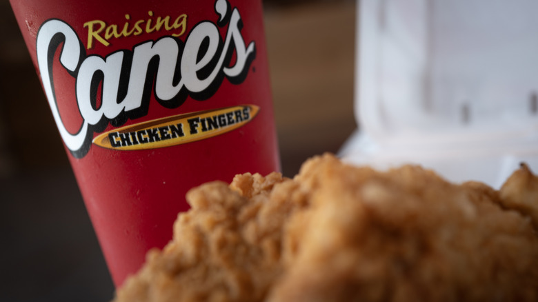 A red cup featuring the Raising Cane's logo, with its signature chicken fingers in front