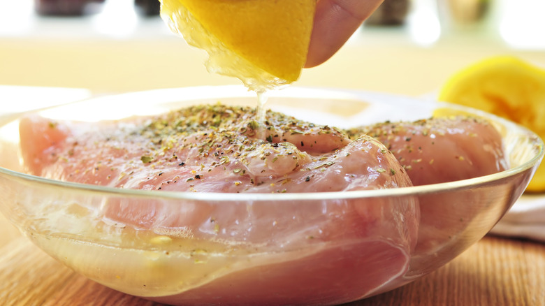 Raw chicken breast in a bowl, with lemon dripping over it for marinating