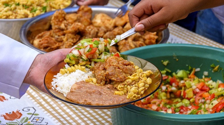 Hand scooping Brazilian food onto a customer's plate.