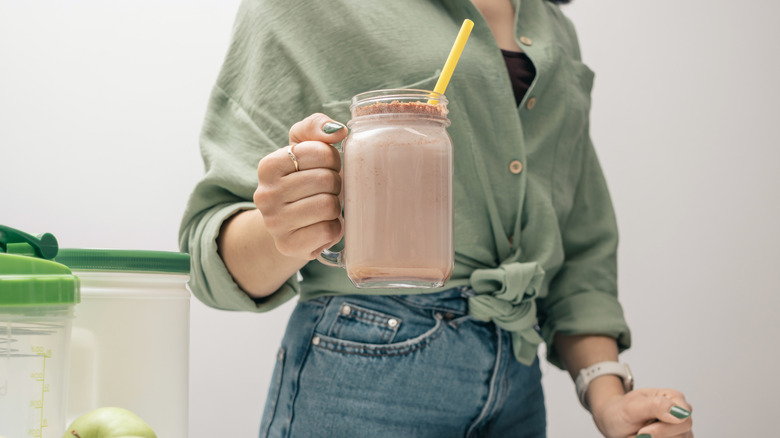 Person in a green shirt and jeans holding a chocolate smoothie