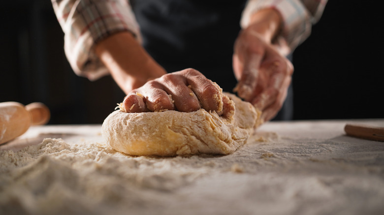 Hands kneading bread dough on floured surface