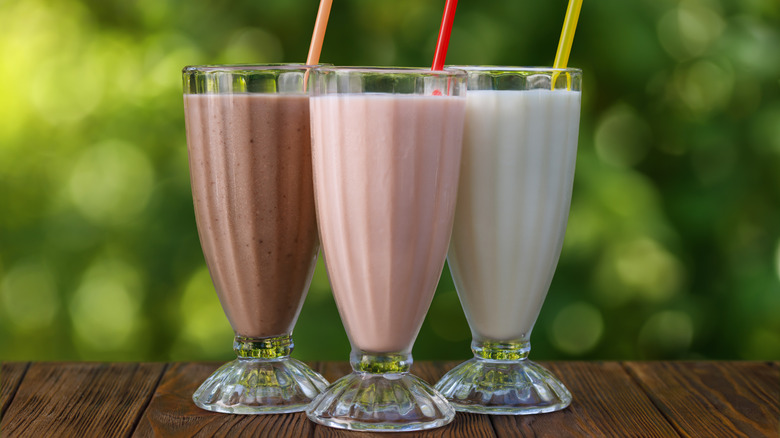 Milkshakes in chocolate, vanilla, and strawberry in tall glasses with straws