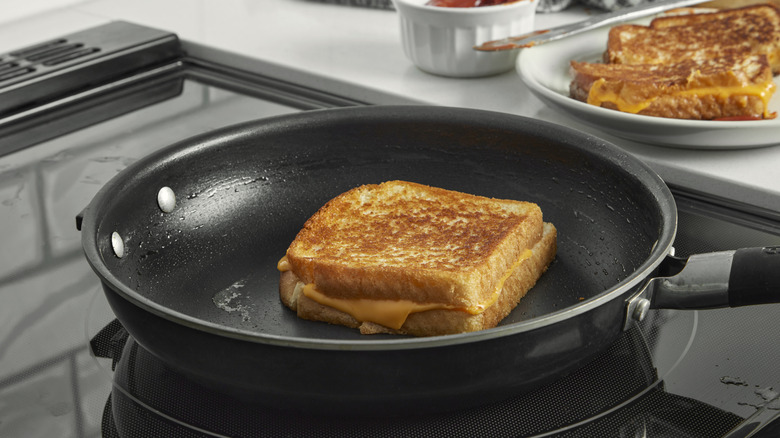 Grilled cheese sandwich cooking in a skillet on a stovetop with melted processed cheese, part of a comfort food series.
