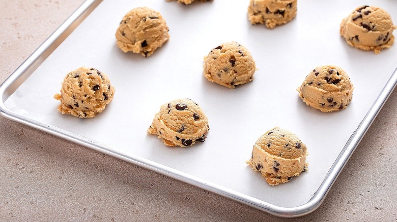 Balls of chocolate chip cookie dough on a metal, parchment-lined baking sheet