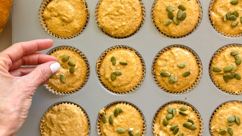 hand adding pumpkin seeds to unbaked muffins