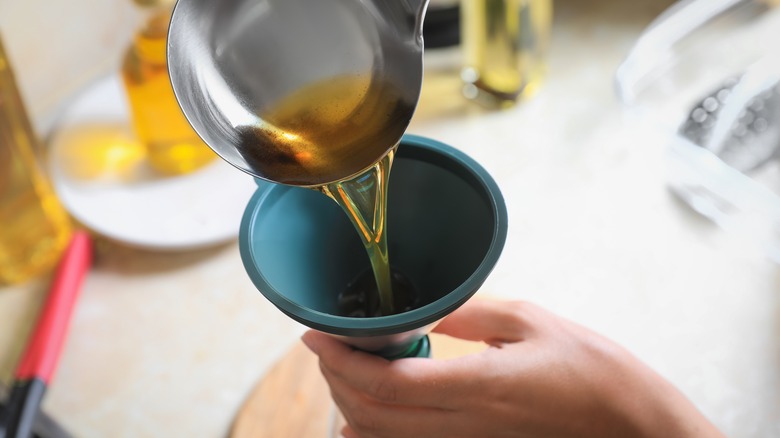 person pouring leftover oil through funnel