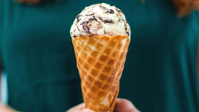 Hands holding a sugar cone with vanilla ice cream and chocolate swirls