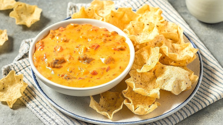 Small bowl of queso on a large white plate with scoop-style tortilla chips