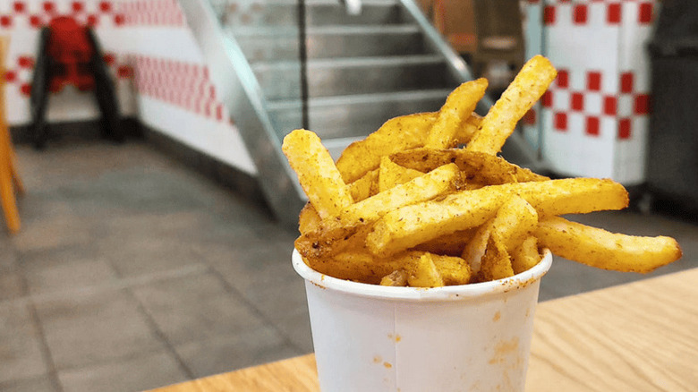 A hand holding a small bag of french fries