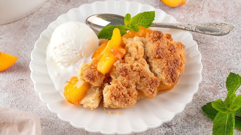 Peach cobbler with a scoop of vanilla ice cream and mint leaves on a white scalloped plate