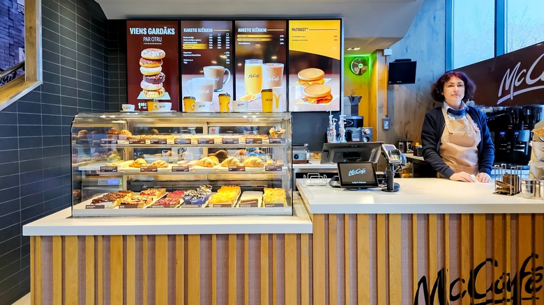 A worker at a McDonald's McCafé service counter with a clear case of pastry items
