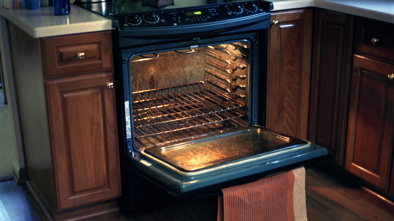 A home kitchen oven door is open to display a heavily used interior.