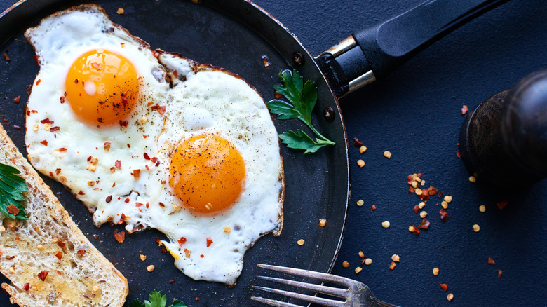 Fried eggs in a pan with chili flakes overtop on black countertop.