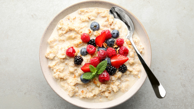 a bowl of oatmeal with strawberries, raspberries, blueberries, blackberries, and a sprig of mint
