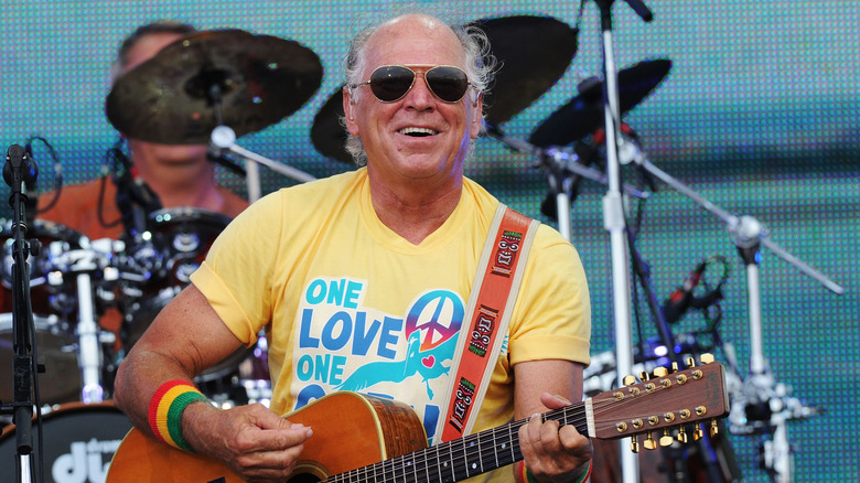 Jimmy Buffett in sunglasses performing with guitar and smiling
