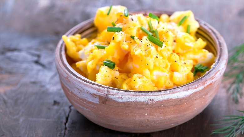 Scrambled eggs with chives and black pepper in a white-washed bowl on a wooden surface