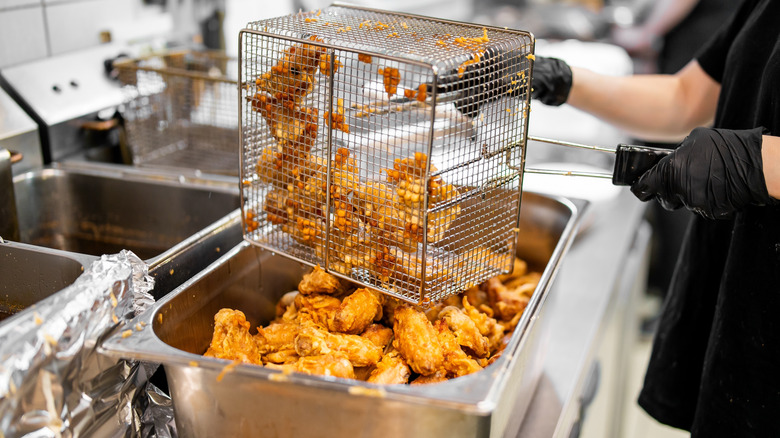 Deep fried chicken being removed from a fryer basket