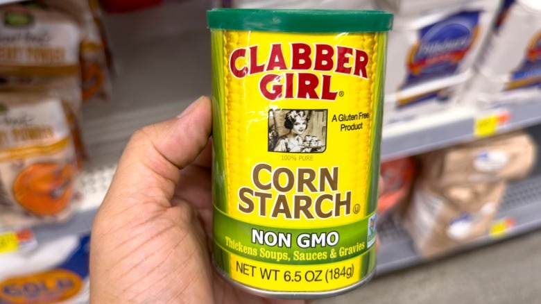 Hand holding cornstarch can in a grocery aisle