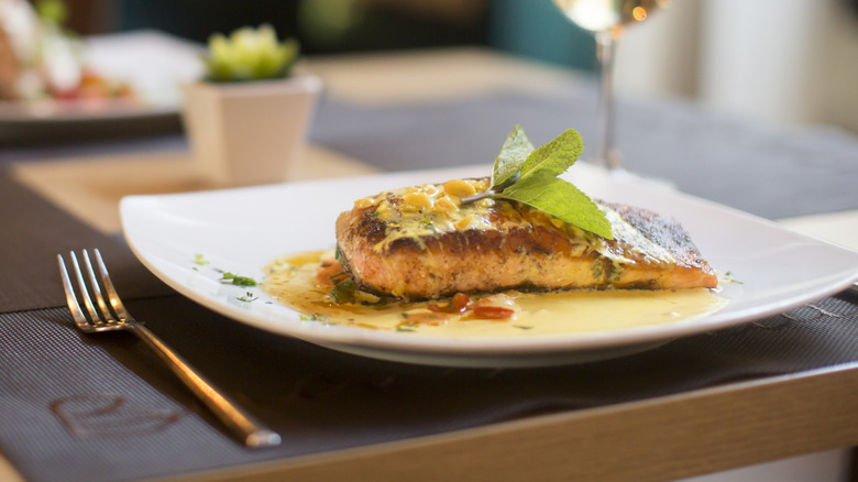 Plate of seared salmon at fine dining restaurant, paired with glass of white wine.