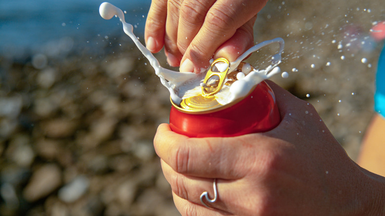 Person opening shaken can of Coke and bubbles exploding out