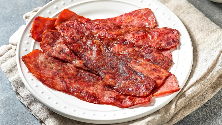 Plate of fully cooked, crispy turkey bacon stacked on a white plate over a cream-colored cloth napkin